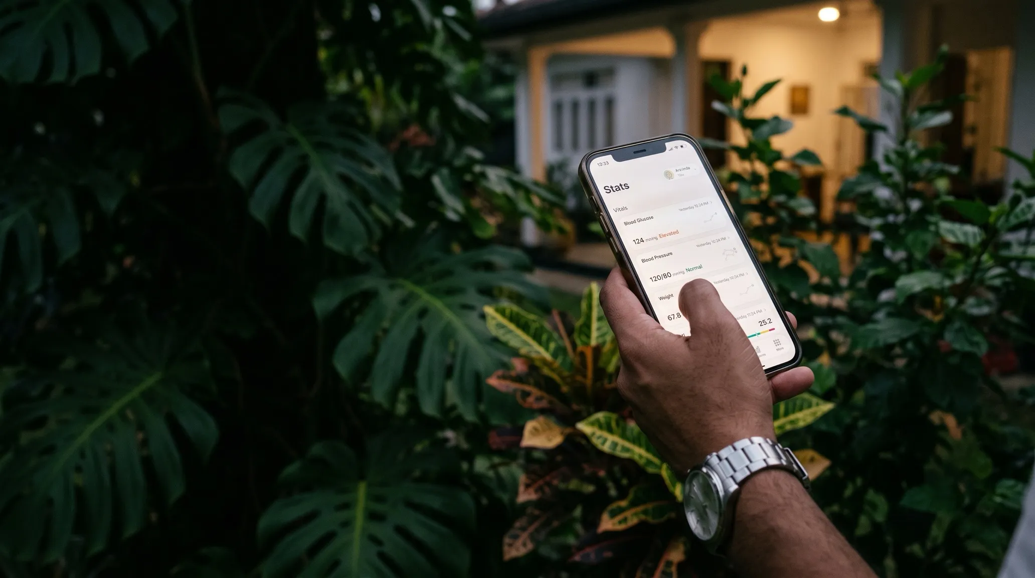 A hand holding a phone showing the Ayubo stats screen, in a garden at dusk